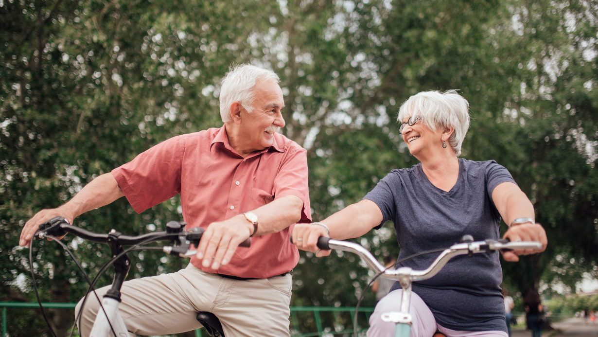 two older adults riding bikes and smiling